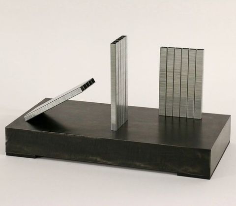 Sculpture. Two panels of staples stand on a black base at right angles to each other. A third angles at about thirty degrees, leaning towards the others.