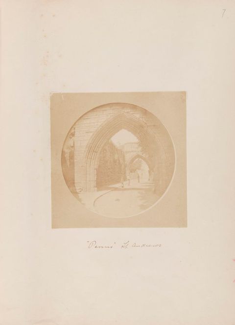 Black and white photograph. In tones of beige and tan, one pointed arch opens onto another, a short distance away down an outdoor path.